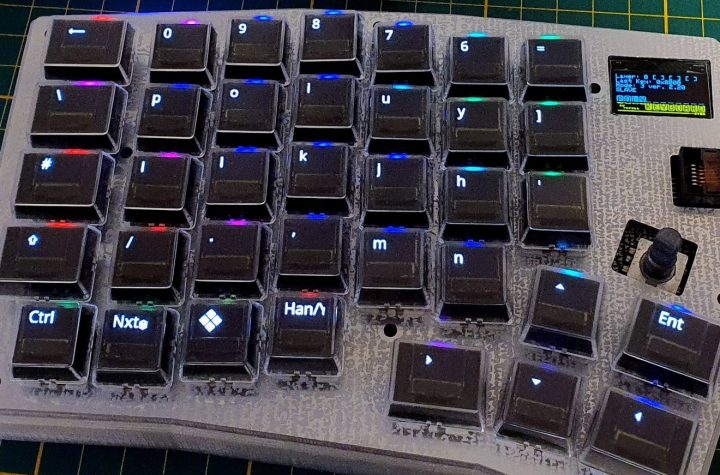 A left-hand side unit of a split keyboard. The keys are black with RGB lighting and the key legends are displayed on small OLED screens in each key.